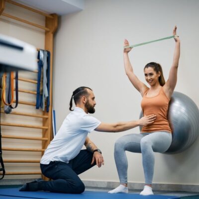 Rehabilitacja: Kobieta wykonuje ćwiczenia z trenerem przy użyciu piłki gimnastycznej.