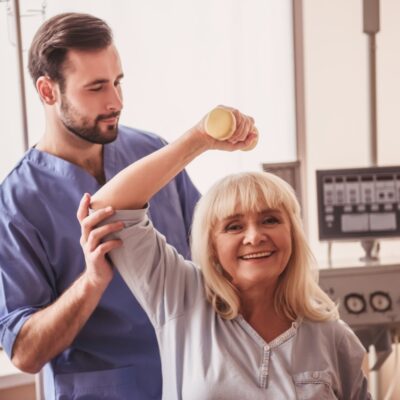 Kobieta uczestniczy w sesji, podczas której terapeuta wykonuje terapię manualną dla jej ramienia.