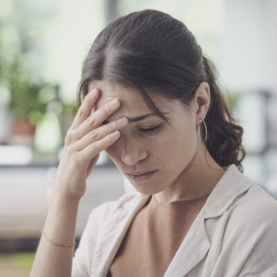 Kobieta trzyma się za czoło, odczuwając bóle głowy.