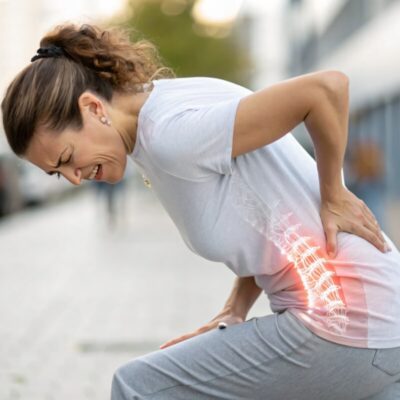 Kobieta na ulicy doświadcza bólu kręgosłupa, trzymając się za dolną część pleców.