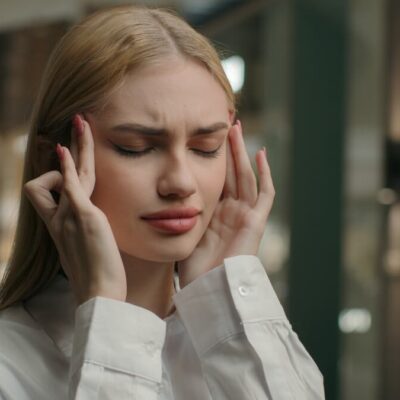 Kobieta z zakrytymi oczami trzyma się za skronie, odczuwając bóle głowy.