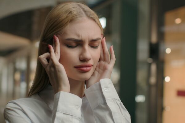 Kobieta z zakrytymi oczami trzyma się za skronie, odczuwając bóle głowy.