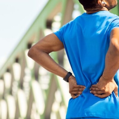 Mężczyzna w niebieskiej koszulce trzyma się za plecy, odczuwając bóle pleców.