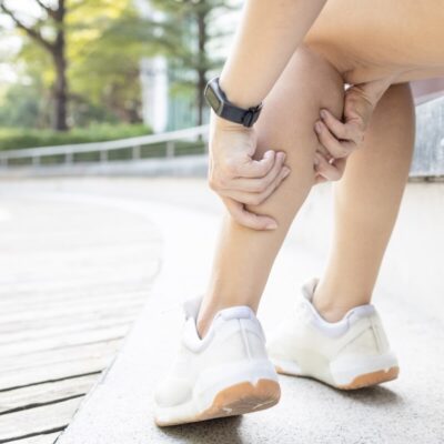 Osoba siedzi na krawędzi i masuje łydkę z powodu drętwienia nóg.